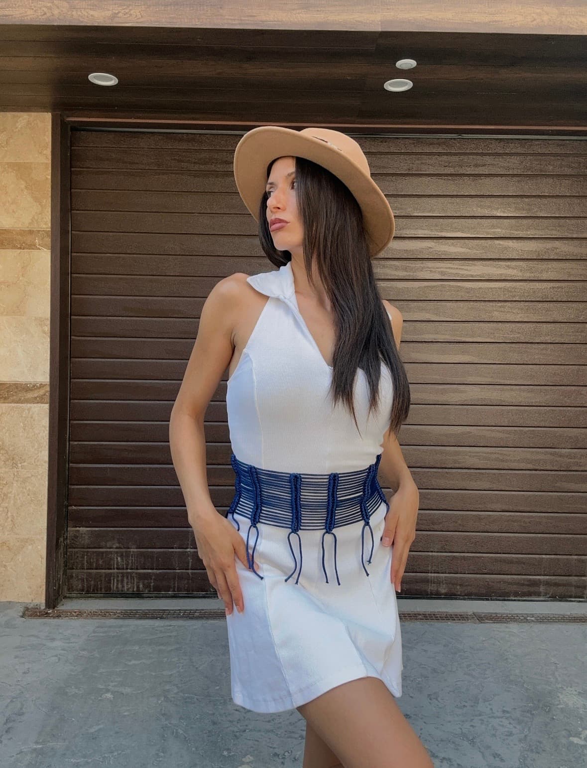 A woman wearing a white dress and wide blue corset belt with a tan hat.